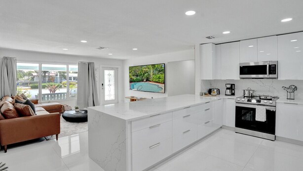 A modern kitchen with white cabinetry, a central island, and a dining area with a brown sofa.
