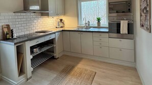 A modern kitchen with white cabinets, a stainless steel range hood, a built-in oven, and a window with a view of trees. - Cozy cottage in top condition close to nature and lakes (Jönköping)