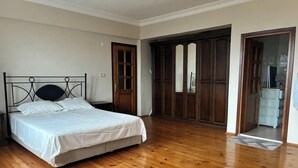 Un dormitorio con suelo de madera, una cama con ropa de cama blanca, un armario de madera y una puerta que da a otra habitación.