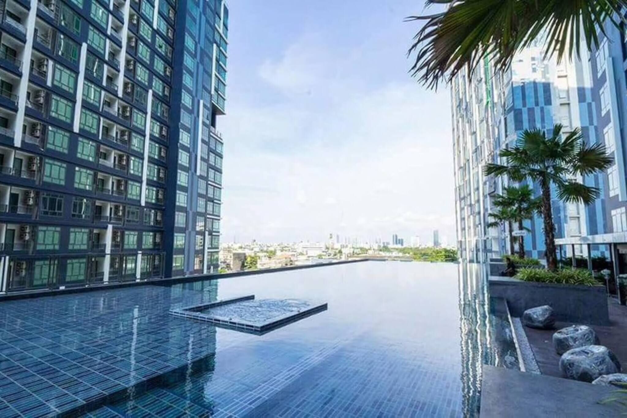 Un bâtiment moderne doté d’une piscine à débordement sur le toit, de grandes fenêtres et de palmiers.