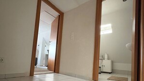 A hallway with white tiled flooring, wooden door frames, and a visible light switch on the wall.