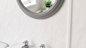 A bathroom with a round mirror, white marble walls, and a sink with two faucets.