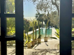 A view through a doorway of a garden with a pool, potted plants, and a pathway.