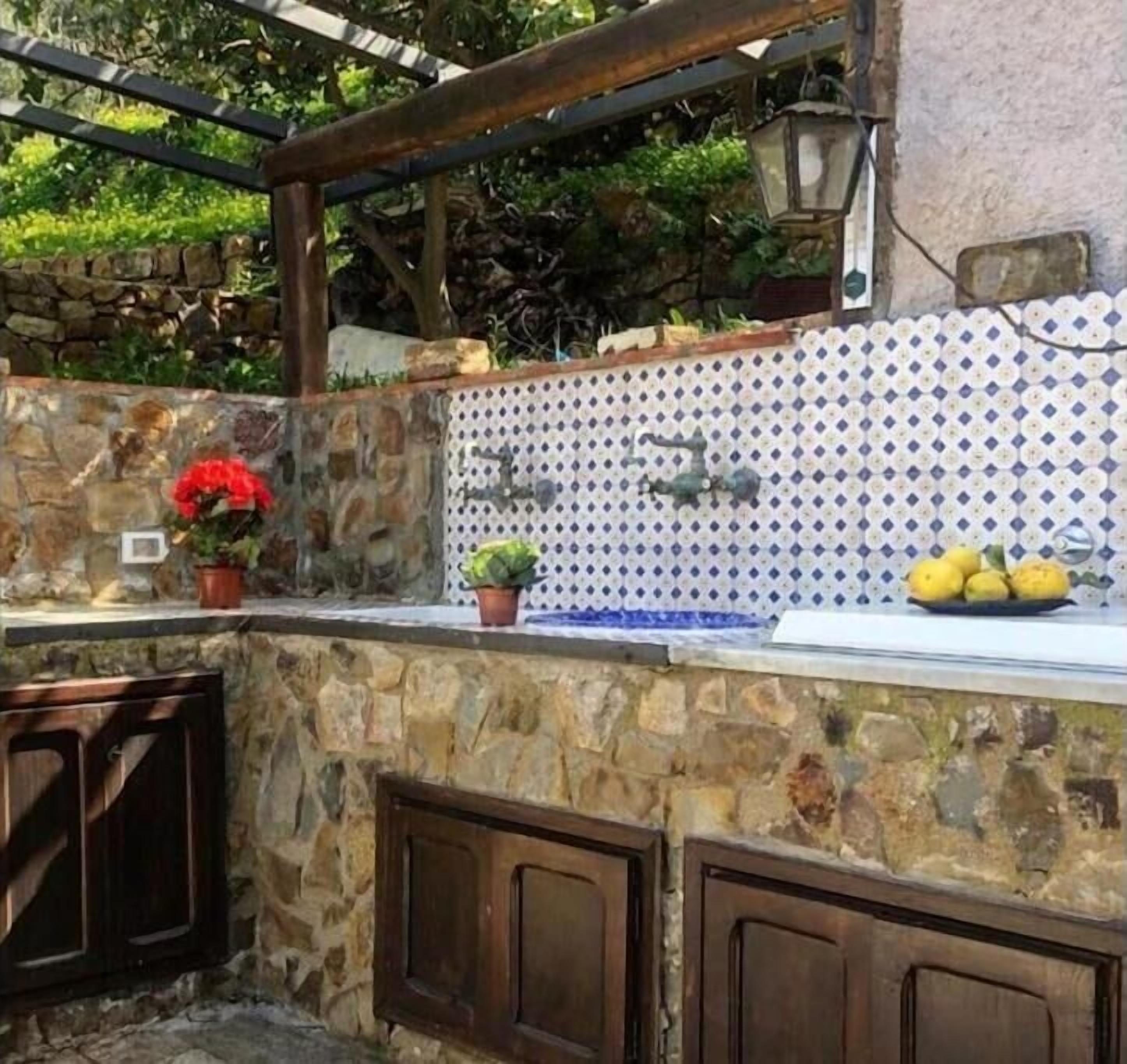 A stone kitchen with a tiled backsplash, a hanging light, and potted plants.