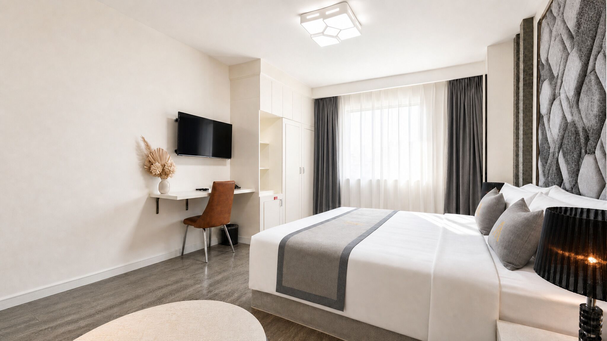 A hotel room with a bed, a desk, a chair, a TV, and a window with curtains.