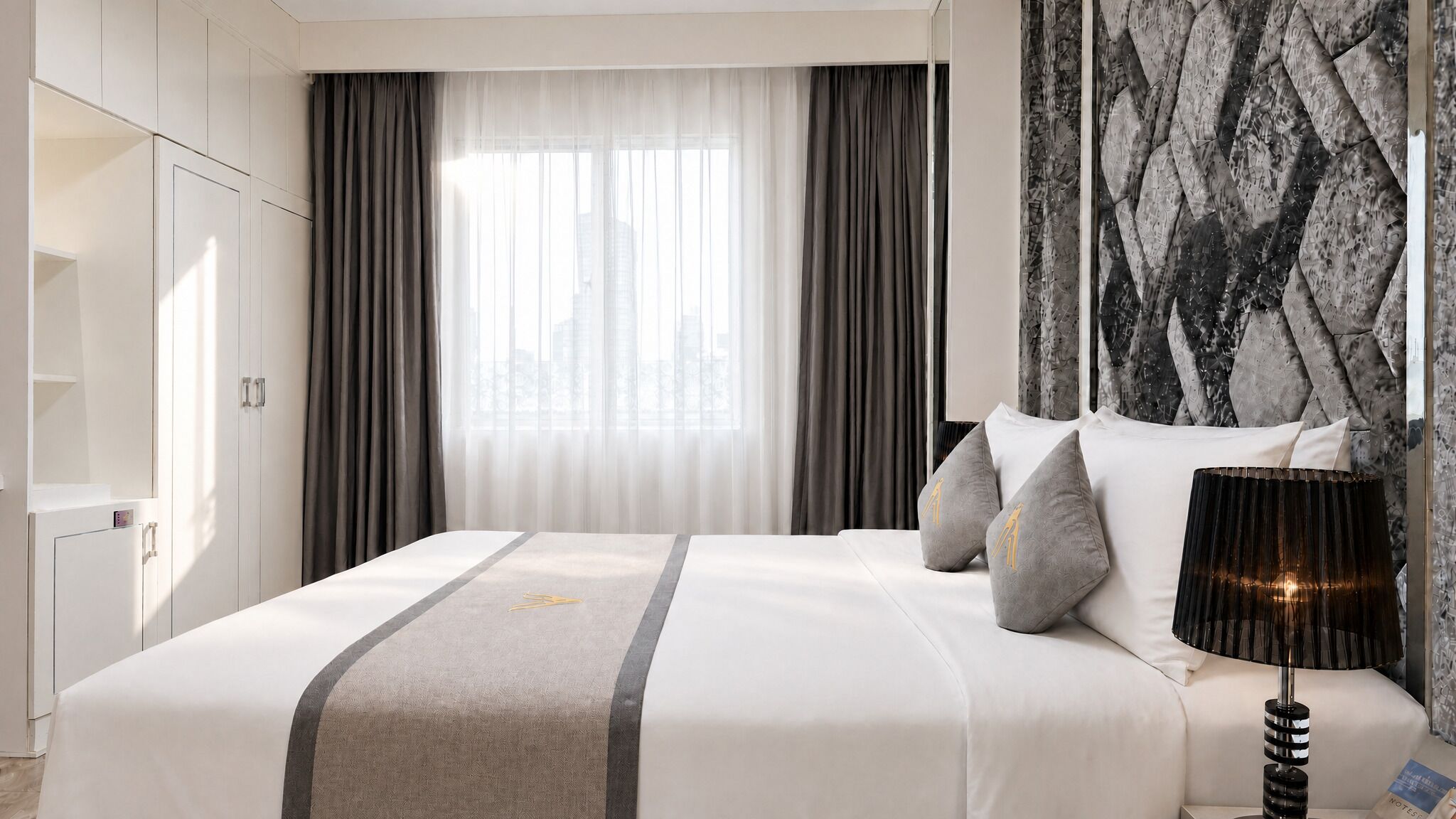 A hotel room with a bed, a nightstand, a lamp, and a large window with curtains.