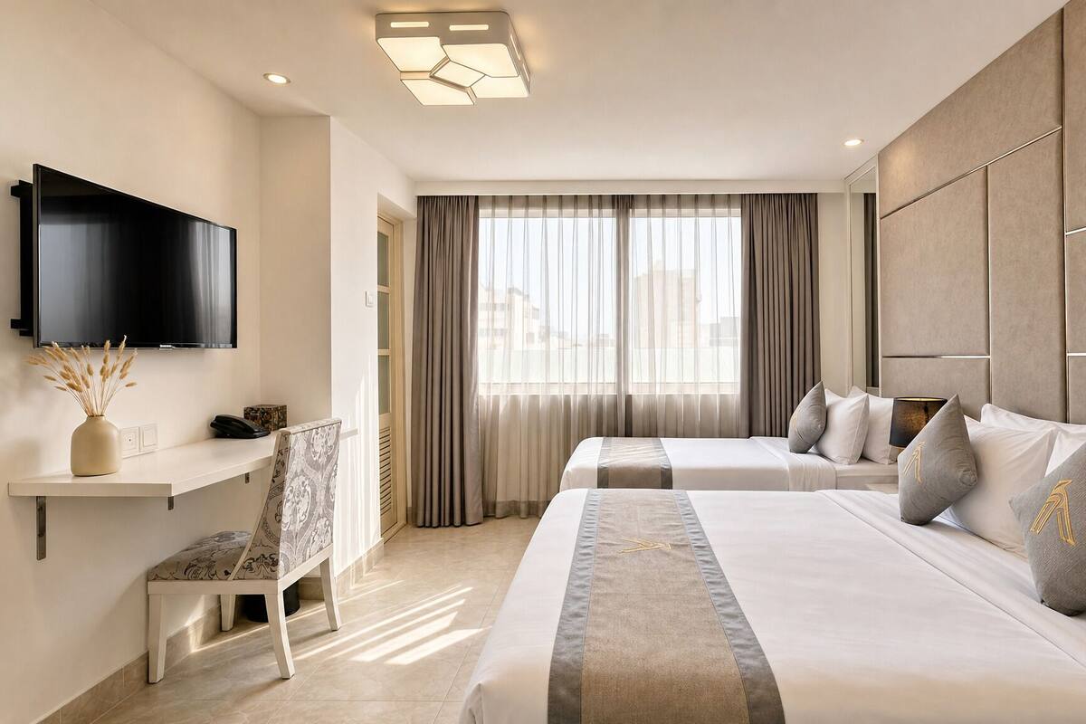 A hotel room with two beds, a TV, a desk with a chair, and a large window with curtains.
