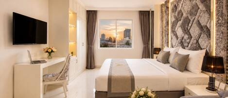 A modern hotel room with a bed, desk, chair, TV, and a city view.