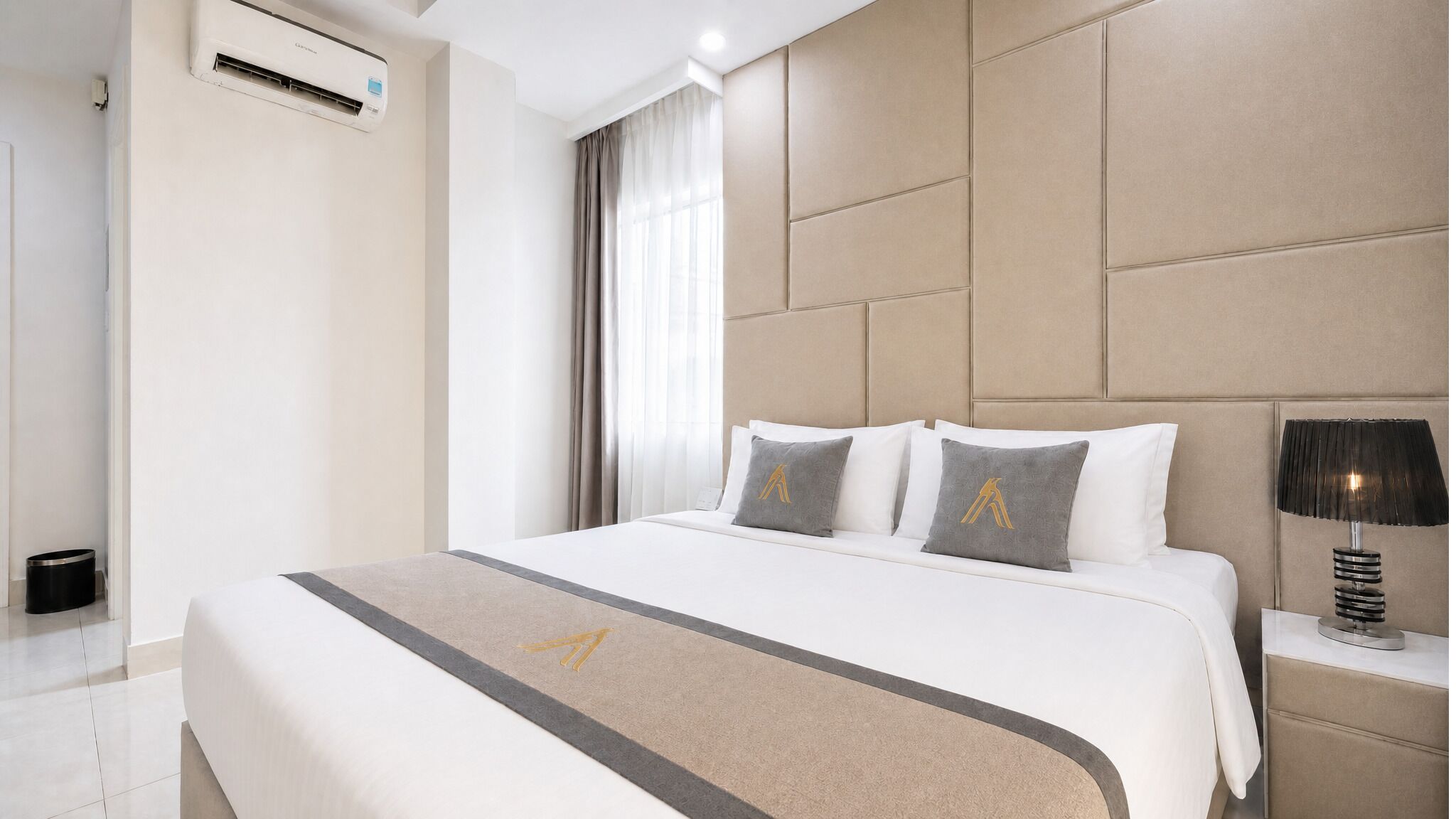 Et hotelværelse med en seng, et natbord, en lampe, en aircondition og et vindue med gardiner.