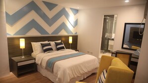 A modern hotel room with a bed, bedside lamps, a shower, a TV, and a mirror. - Bryan Condominium Suites (Makati)