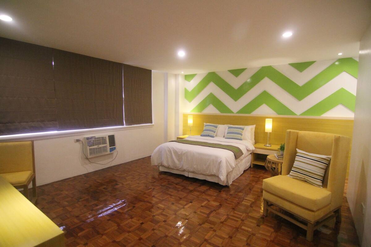 Een hotelkamer met een bed, een stoel, een nachtkastje en een wandairconditioner.