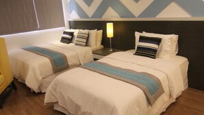 A hotel room with two beds, a wooden floor, a chevron-patterned wall, and a nightstand with a lamp. - Bryan Condominium Suites (Makati)