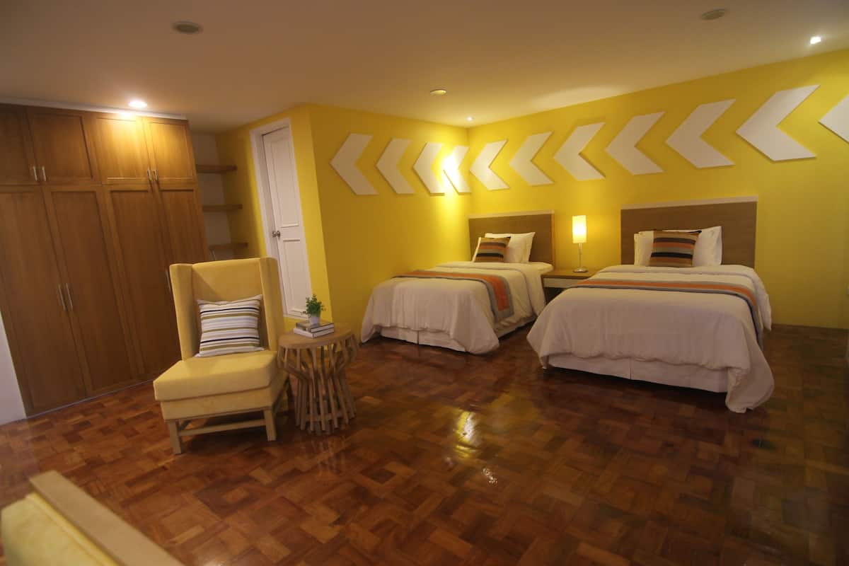 Een hotelkamer met twee bedden, een stoel, een tafeltje en houten vloeren.