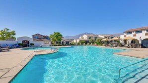 Ein Swimmingpool mit klarem, blauem Wasser, umgeben von Liegestühlen und Sonnenschirmen, mit Blick auf dahinterliegende Bergketten.