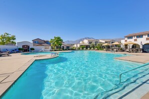 Ein Swimmingpool mit klarem, blauem Wasser, umgeben von Liegestühlen und Sonnenschirmen, mit Blick auf dahinterliegende Bergketten.
