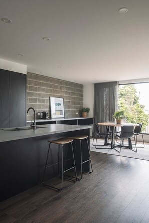 A modern kitchen with a dark backsplash, a central island with stools, and a dining area with a view. - Downtown House in Geelong (Geelong)