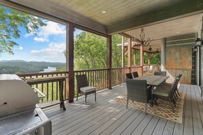 A covered outdoor deck with a grill, wicker furniture, and a view of a lake and mountains. - Luxurious Mtn Retreat w/ Lake Glenville Views! (Glenville)