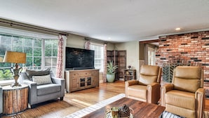 A living room with a TV, leather chairs, a wooden coffee table, and a brick wall. - Close to Intel/Nike: Large Family Home w/ Hot Tub (Aloha)
