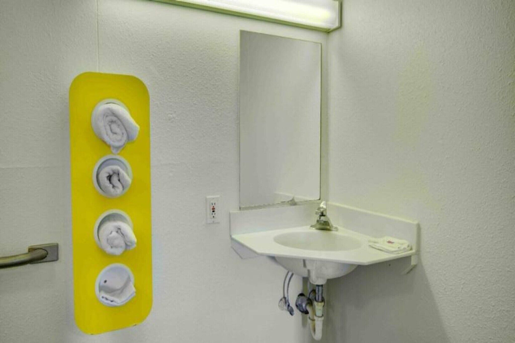 A bathroom with a white sink, a mirror, and a yellow towel dispenser with four towels.