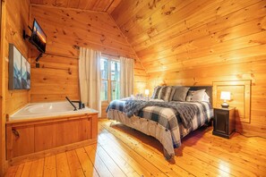 Ein Schlafzimmer einer Holzhütte mit einem Bett, einem Nachttisch, einer Lampe, einem Fenster und einer Holzwanne.