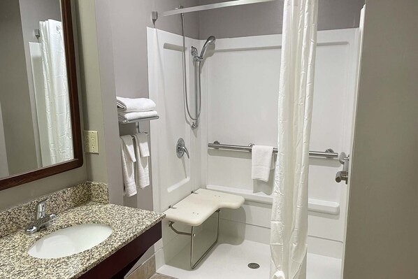 A bathroom with a granite countertop sink, a shower with a grab bar, and a mirror with a wooden frame.