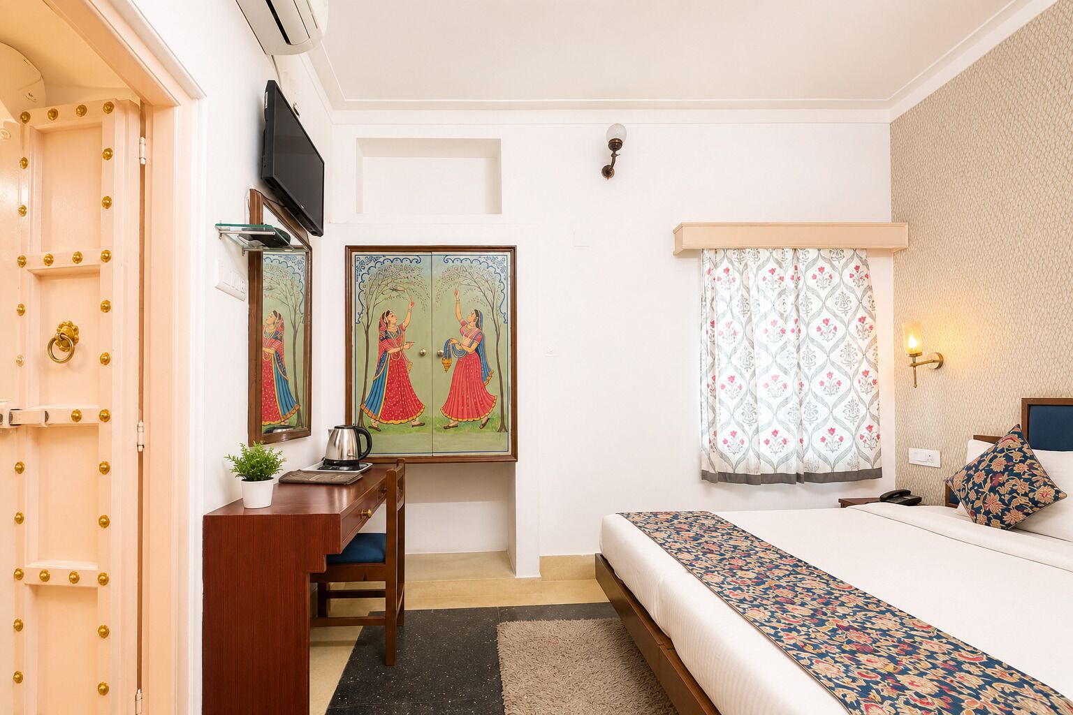 A bedroom with a bed, a desk with a chair, a television, and a window with curtains.