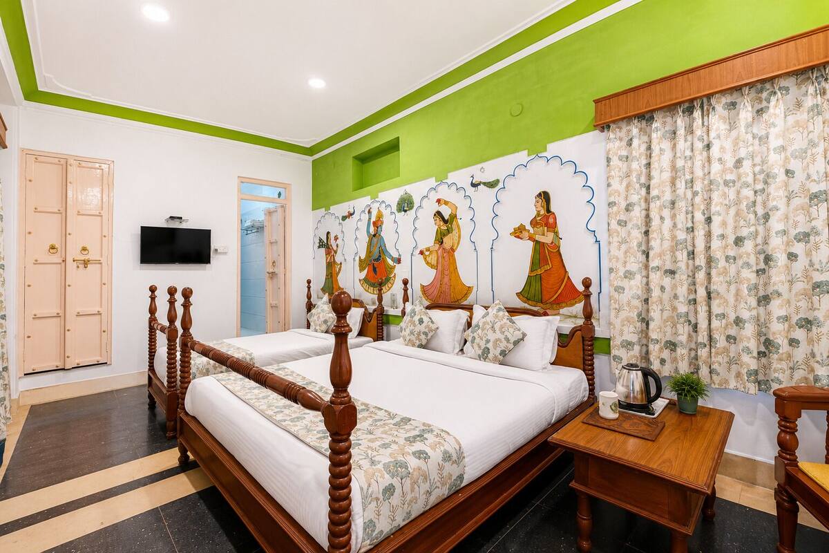 A hotel room with a large bed, a wooden nightstand, a television, and a green accent wall.