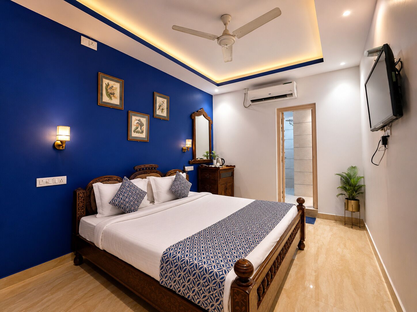 A bedroom with a bed, a ceiling fan, an air conditioning unit, a television, and framed pictures on the wall.