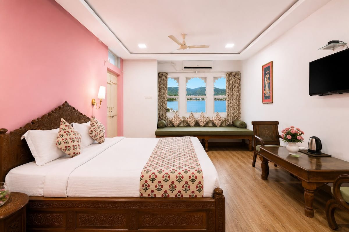 A bedroom with a bed, a desk, a chair, a television, and a window with a view of the sea.