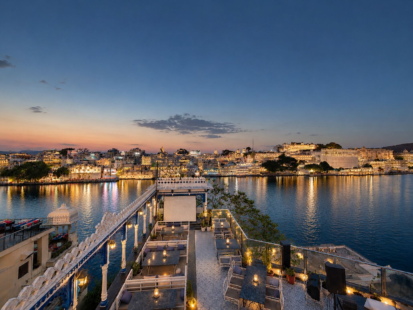 A waterfront restaurant with outdoor seating overlooking a cityscape at dusk.