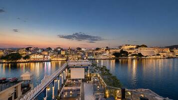 A waterfront restaurant with outdoor seating overlooking a cityscape at dusk.