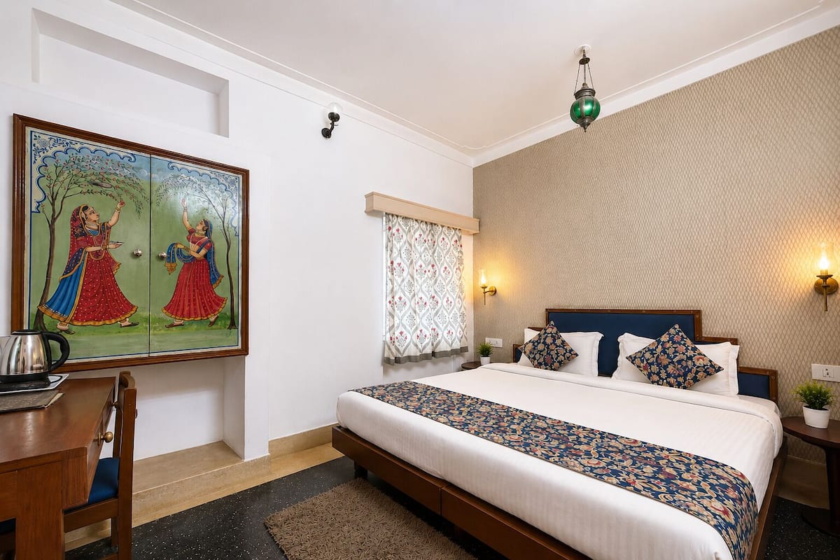 A hotel room with a bed, a desk, a painting, a window with patterned curtains, and a textured wall.