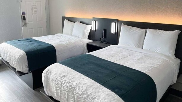 Habitación de hotel con dos camas, una mesita de noche, teléfono en la pared y una puerta con cerradura.