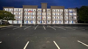 Un hotel de varios pisos con un estacionamiento al frente, que indica 'ABIERTO AHORA'.