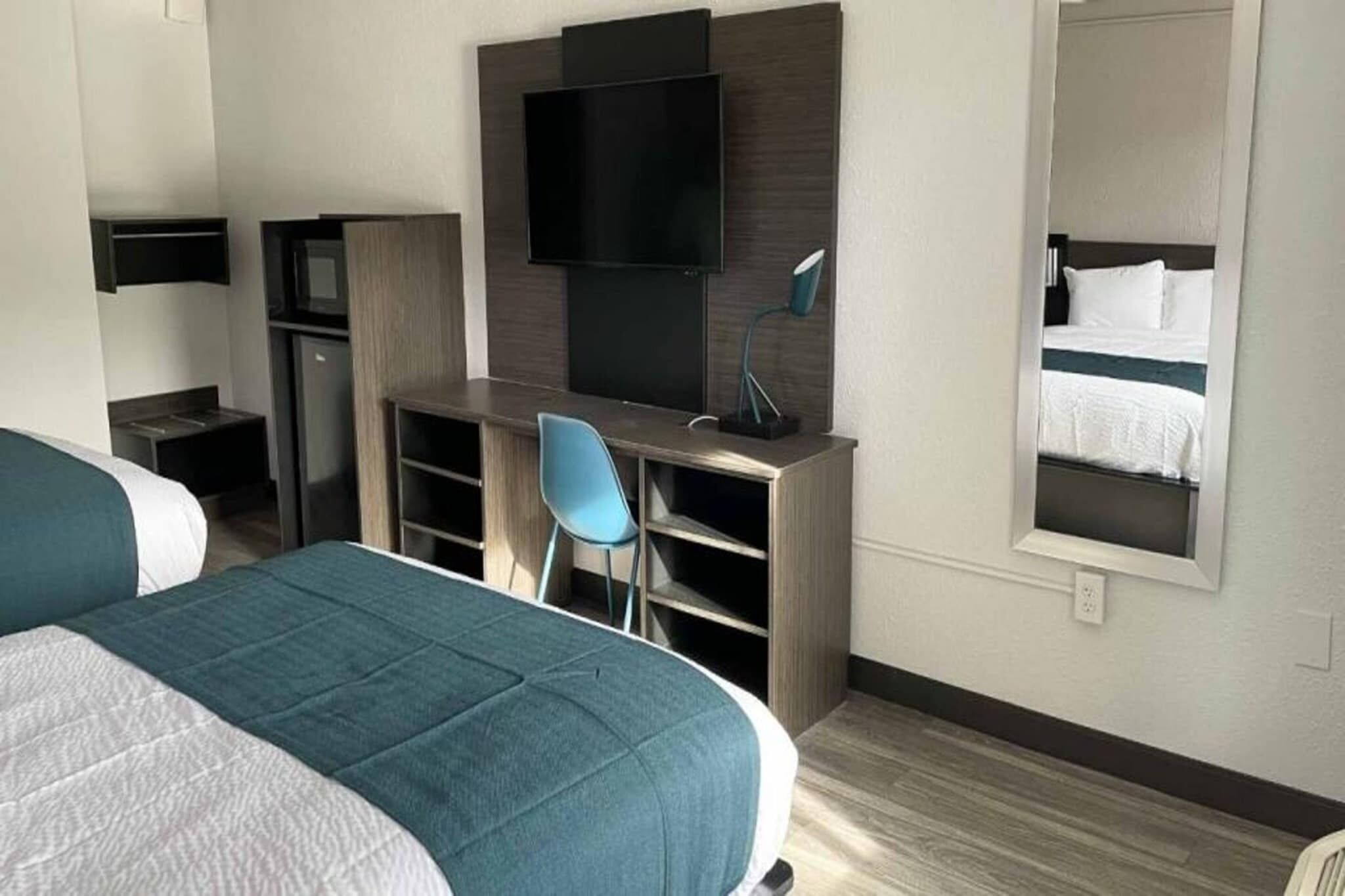 Une chambre d’hôtel avec deux lits, un bureau avec une chaise, une télévision et un miroir.