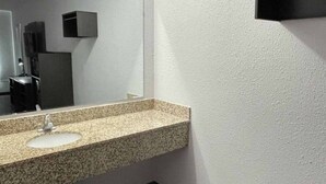 Une salle de bain avec un lavabo doté d’un plan de travail en granit, un miroir et un distributeur de savon fixé au mur.