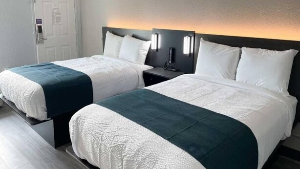 Une chambre d’hôtel avec deux lits, une table de chevet et un luminaire fixé au mur.