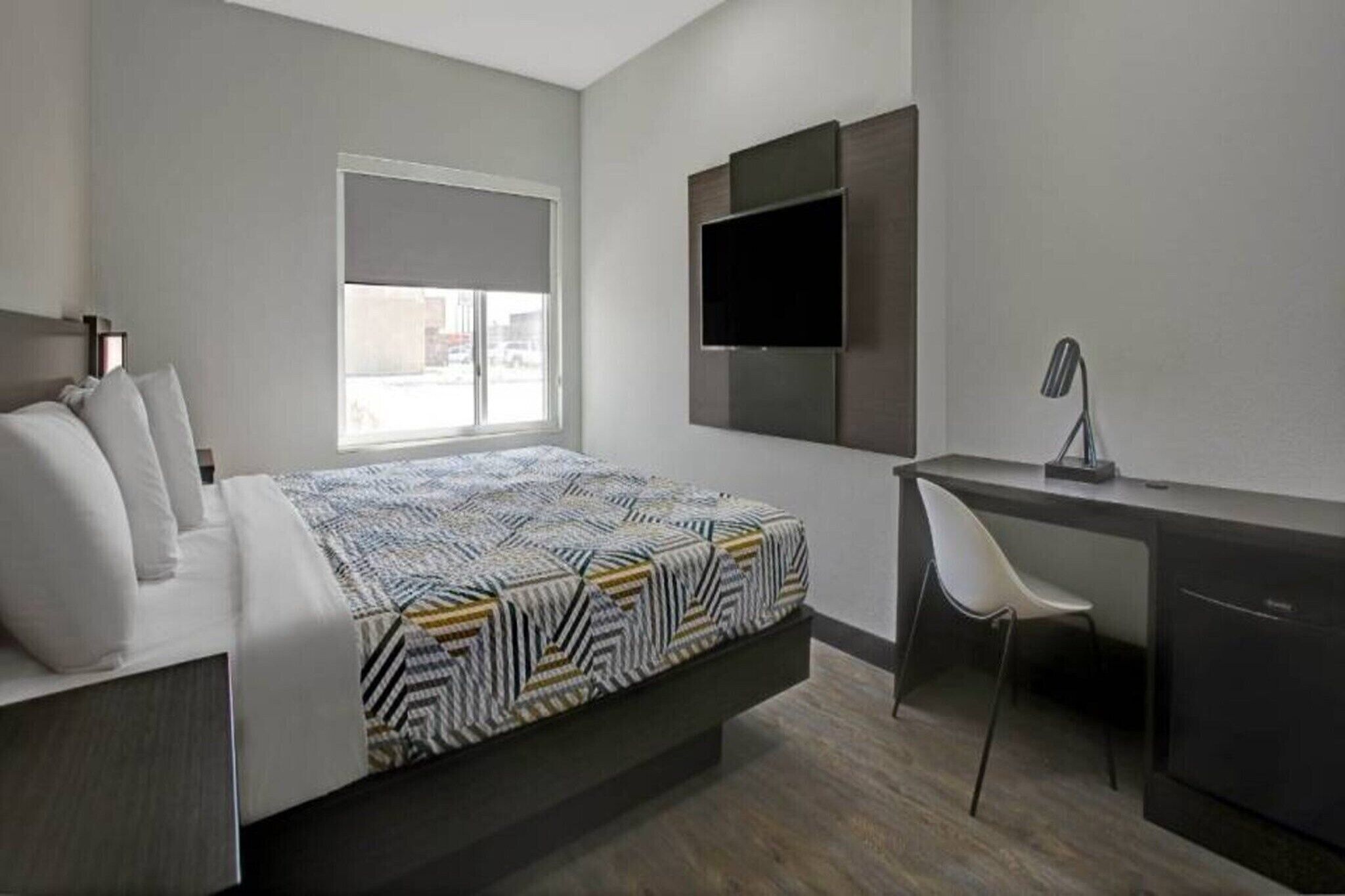 Ein modernes Hotelzimmer mit Bett, Schreibtisch, Stuhl, Fernseher und Fenster.