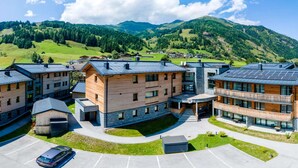 A modern hotel complex with multiple buildings, a parking area, and a mountainous backdrop. - Rauris Penthouse with Sauna (Rauris)
