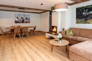 Ein modernes Wohnzimmer mit Holzboden, einer Couch, einem Esstisch mit Stühlen, einem Kamin und einem Bild an der Wand.