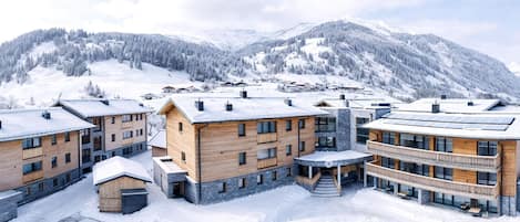 A modern hotel complex with multiple buildings, a parking area, and a mountainous backdrop.