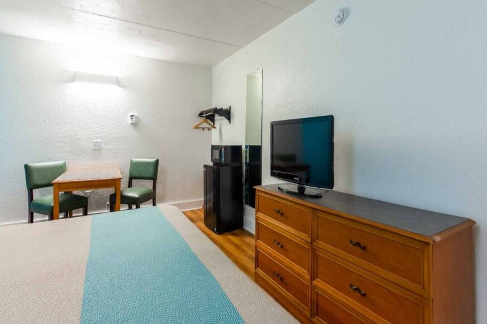 Ett rum med en tv, en byrå, ett bord med stolar och en lampa.