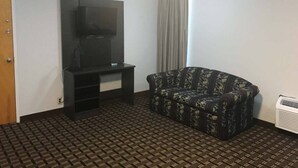 A room with a television on a stand, a patterned sofa, a door, and a patterned floor.