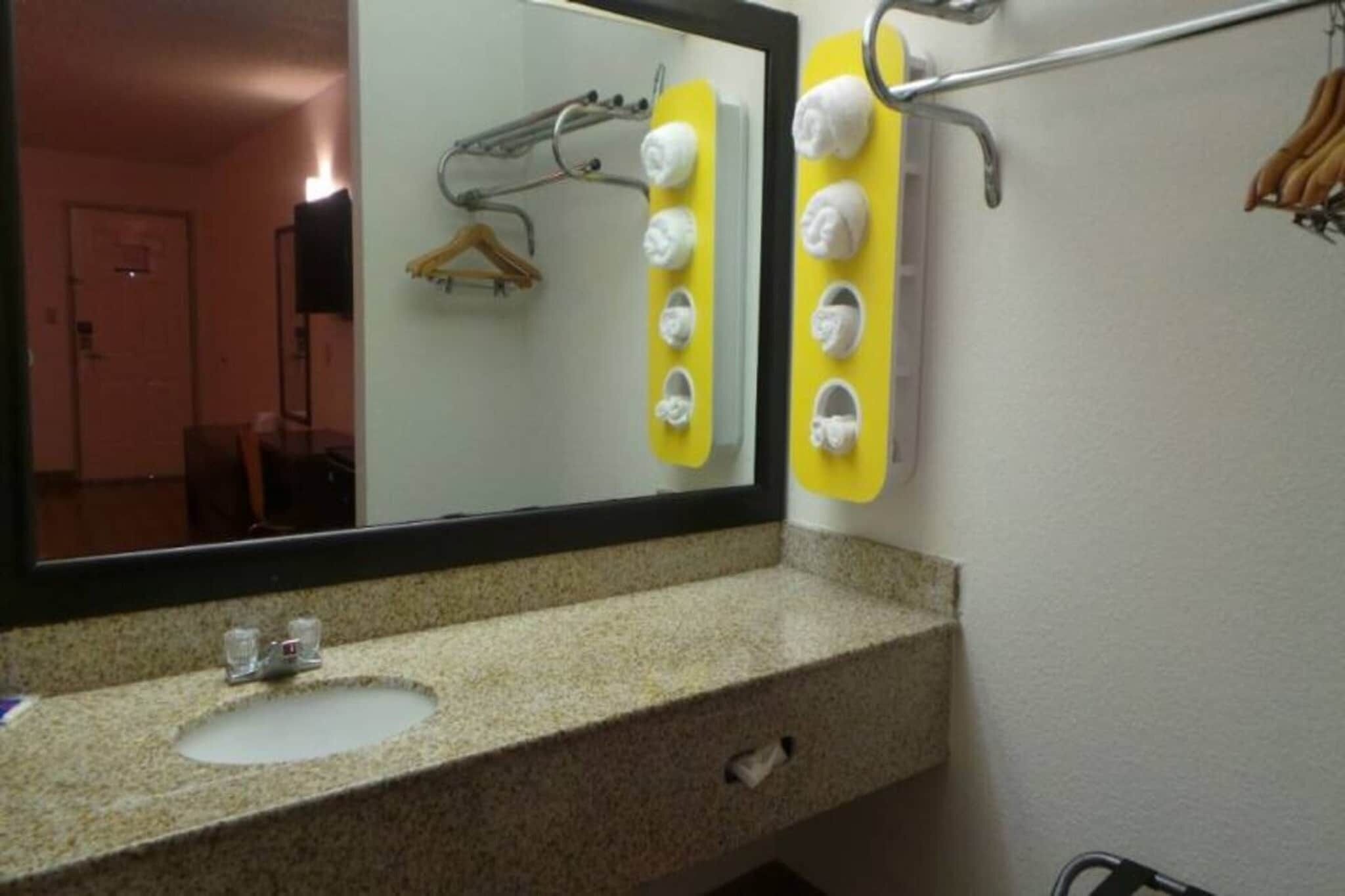 A bathroom with a granite countertop, a sink, a mirror, and a towel rack with multiple towels.