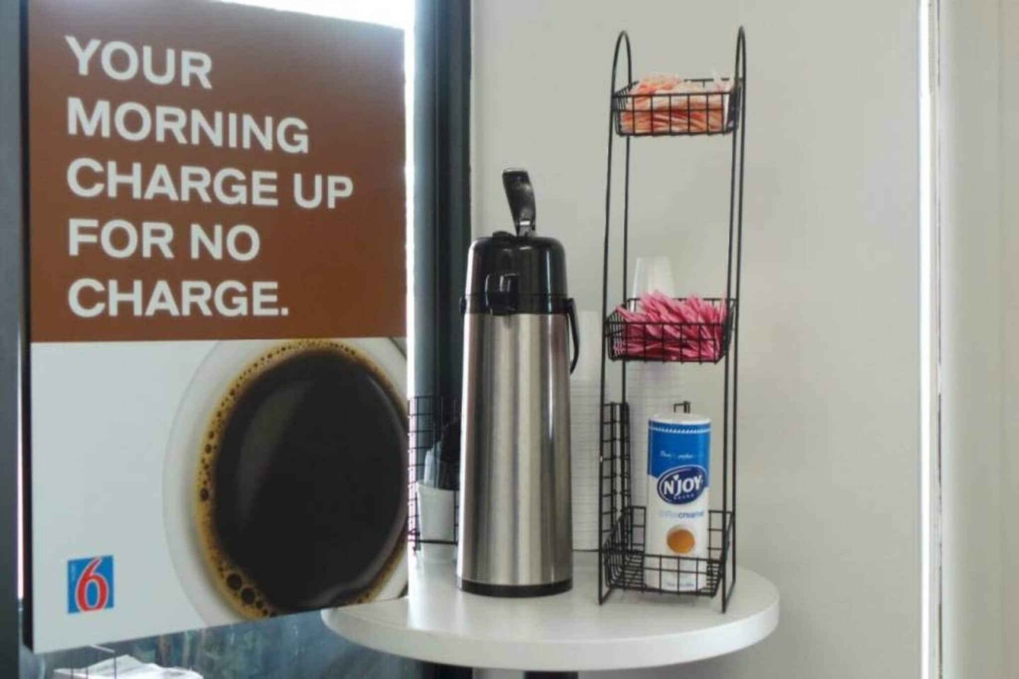 Una cafetera, una taza y un producto de limpieza sobre un estante blanco.
