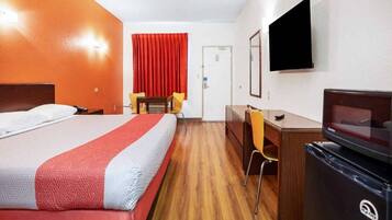 Quarto de hotel com cama, escrivaninha, cadeira, televisão e frigorífico.