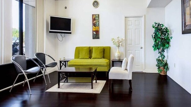 A living room with a green sofa, a flat-screen TV, a white door, and a potted plant.