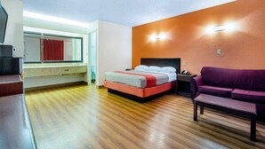 A hotel room with a bed, a sofa, a TV, and a window with a red curtain.
