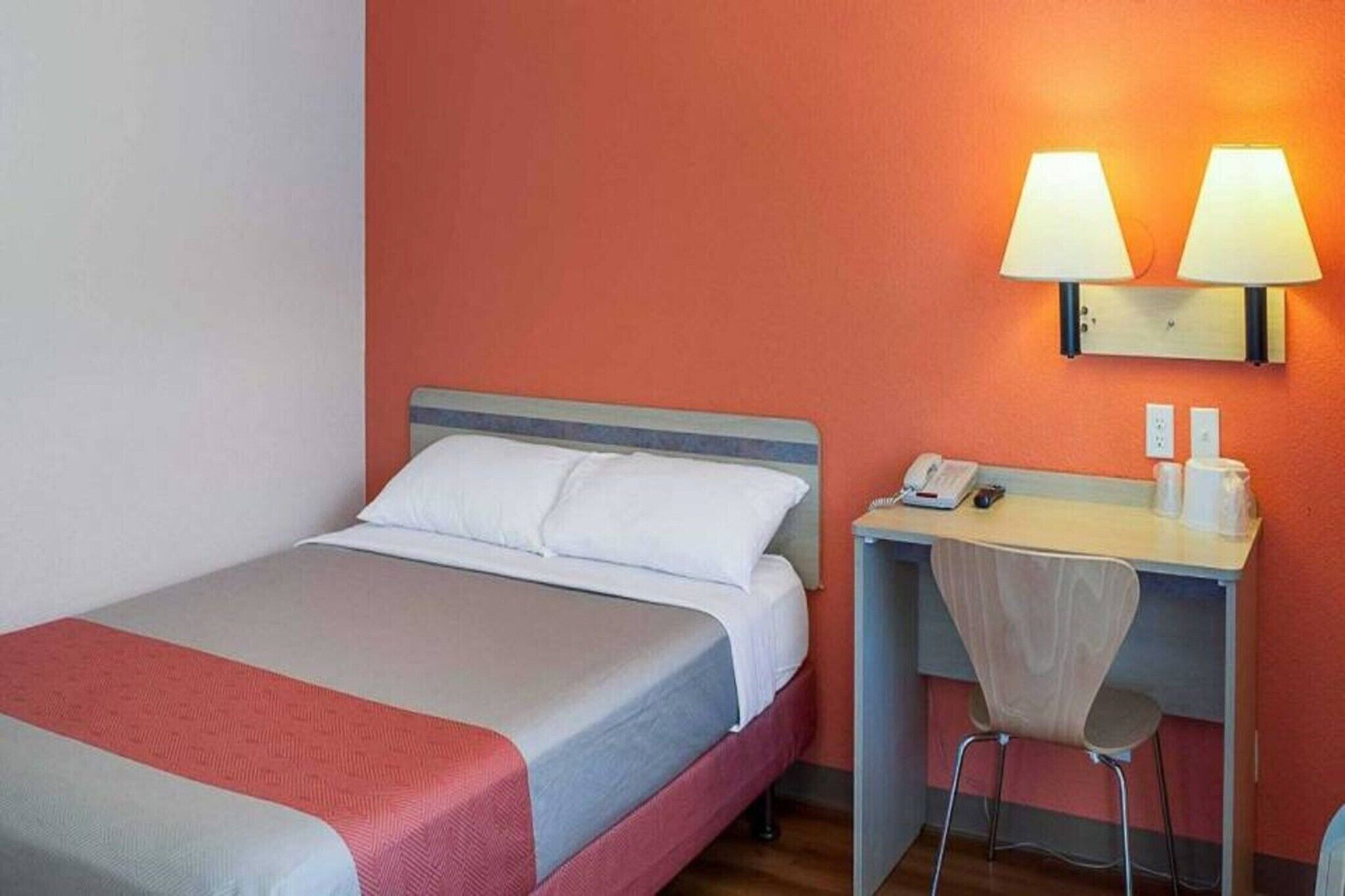Ein Hotelzimmer mit Bett, Schreibtisch, Stuhl und zwei Wandlampen.