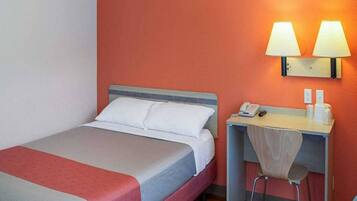 Ein Hotelzimmer mit Bett, Schreibtisch, Stuhl und zwei Wandlampen.